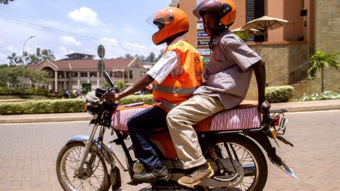 Pioneer moto-taxi ride hailing firm; SafeBoda has been in the business since 2014. A rider is seen wearing a reflective jacket, and helmet carrying an extra one passenger who does have a helmet as well.(Photo Credit: Technology Review)