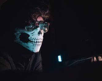 A hacker in a dark room with a covered face typing away at a computer trying to steal personal information or hack into a system is a cybersecurity threat. PHOTO: Nahel Abdul Hadi/Unsplash