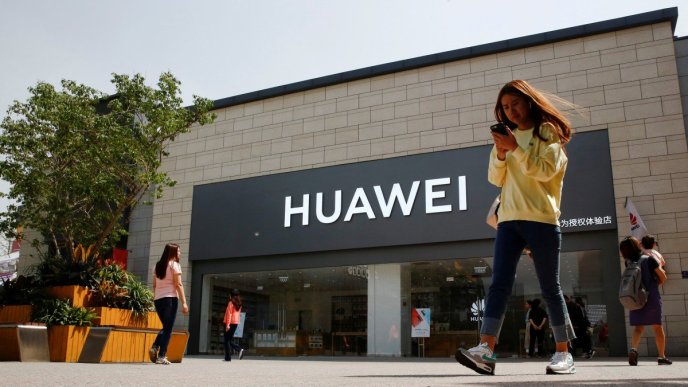 A woman looks at her phone as she walks past a Huawei shop in Beijing. Courtesy Photo/Reuters