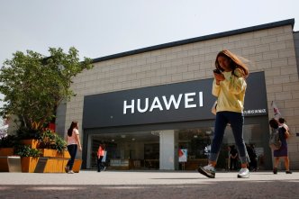 A woman looks at her phone as she walks past a Huawei shop in Beijing. Courtesy Photo/Reuters